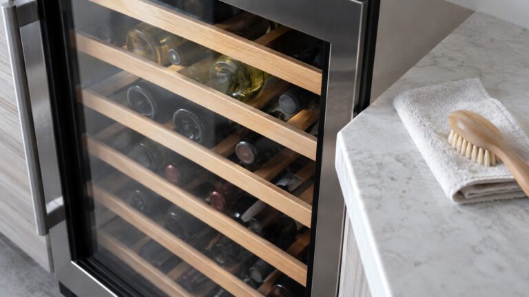 Close-up of the glass door and wooden shelves of a wine cabinet mid-clean, with a cloth and a brush on the counter beside it, seen from slightly above, with nothing else in the frame.
